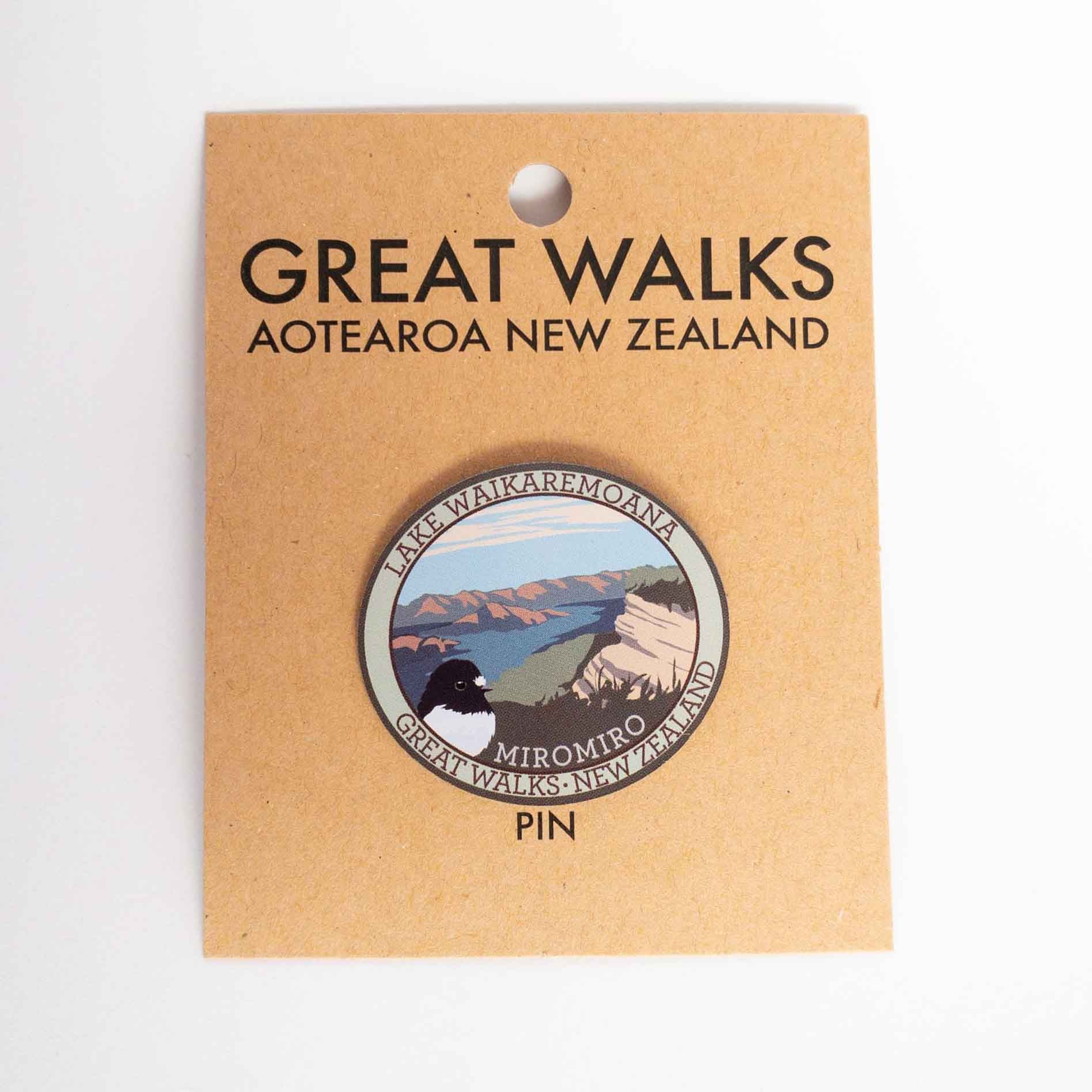 Oval Lake Waikaremoana Track pin, with a miromiro/tomtit bird, blue sky, hills and blue lake, on brown kraft backing card.